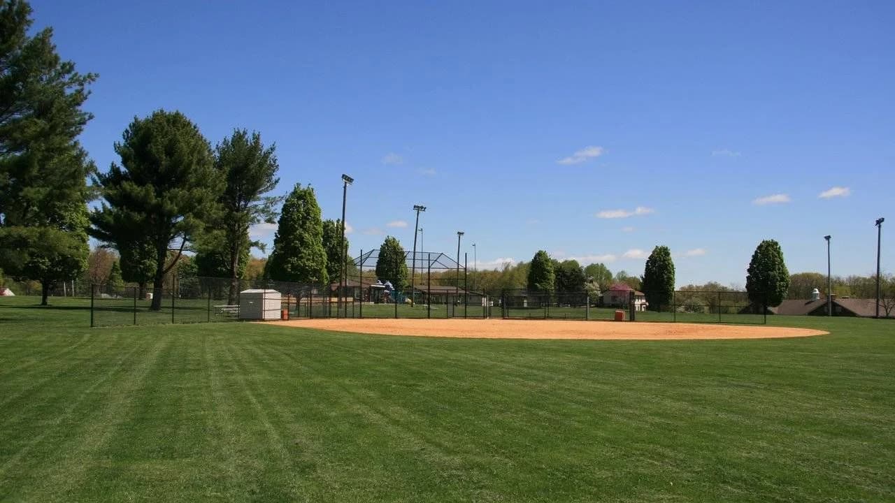 Empty softball diamond with dirt infield and green outfield under a blue sky; no people visible