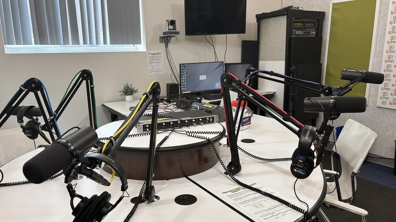 A podcast studio with professional microphones on boom arms around a table; no people present.
