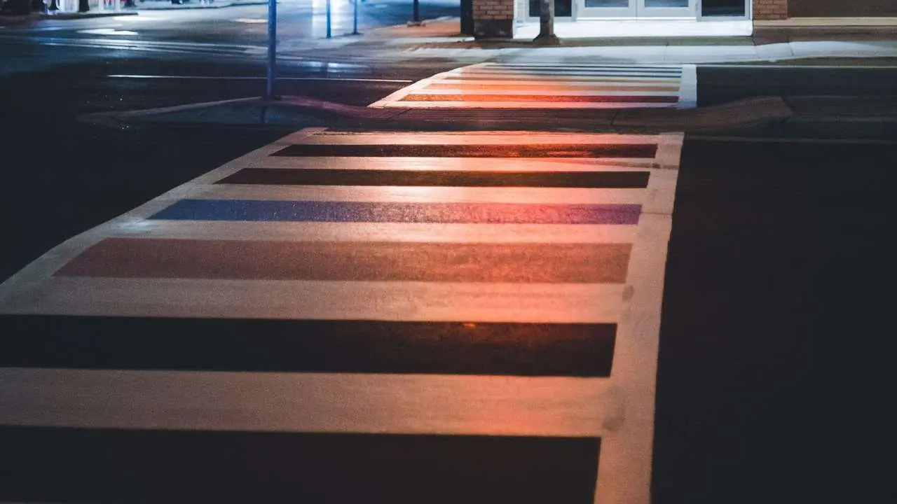 Night-time city intersection with a marked crosswalk under the glow of a traffic light; no people or vehicles visible.