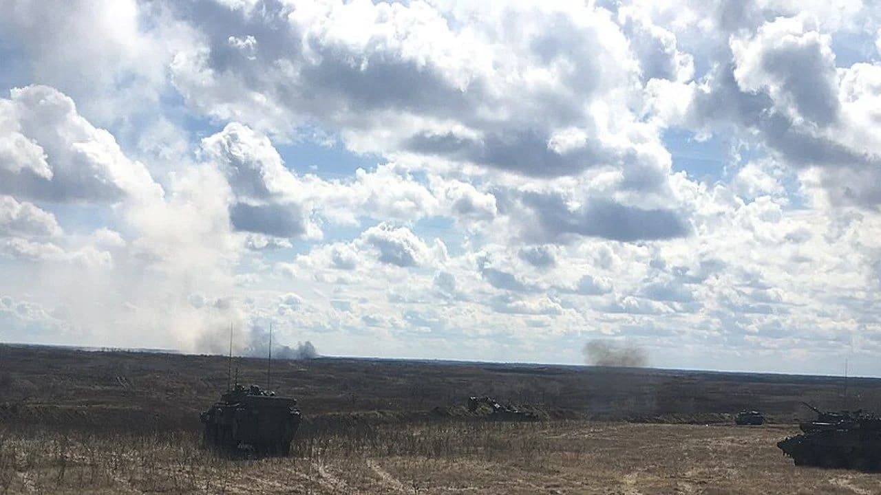 Smoke rising on the horizon of the CFB Wainwright training area with armoured vehicles in the foreground