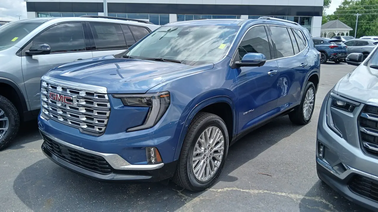 A blue GMC Acadia Denali SUV parked among other vehicles on a dealership lot; no people visible.