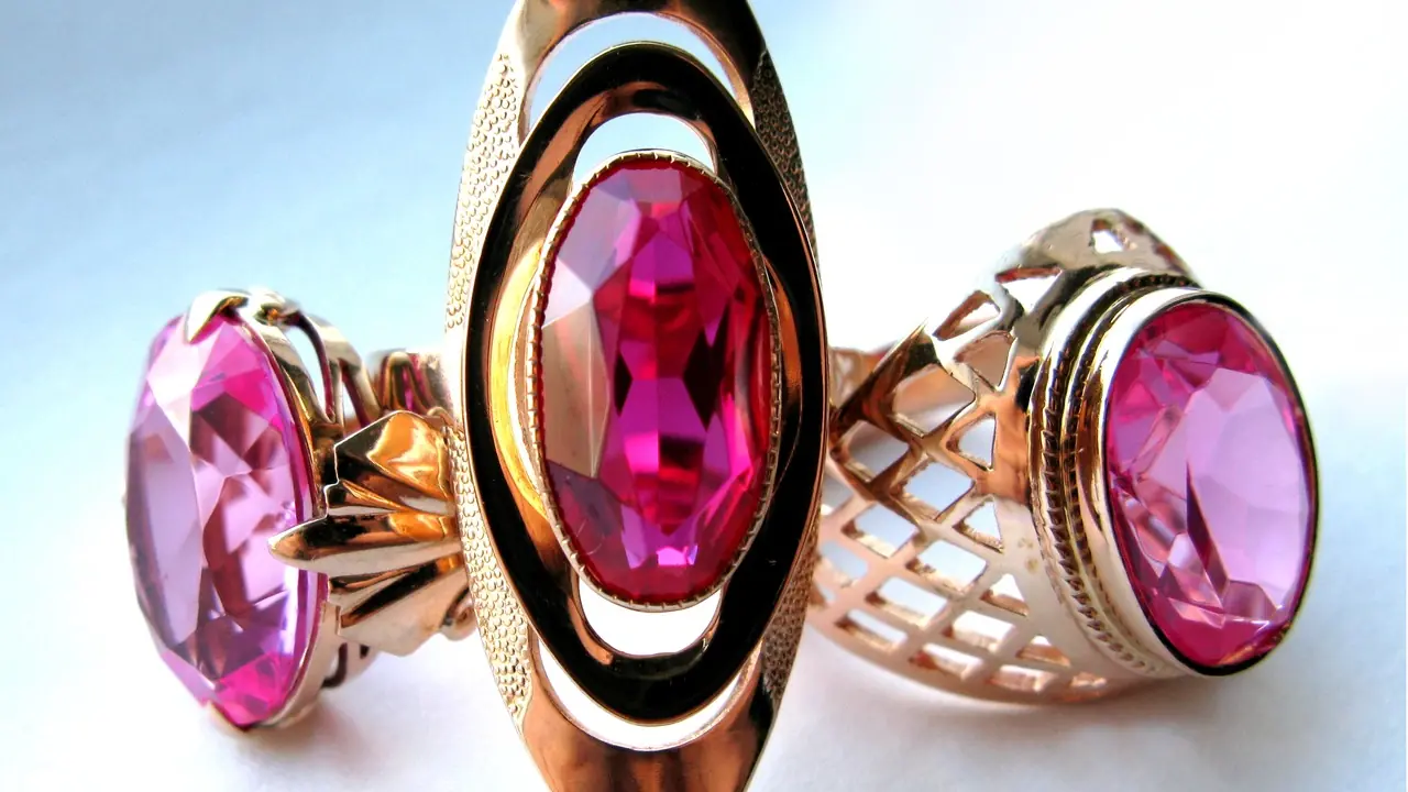 Three gold rings set with large pink stones, photographed close up against a pale background; no people visible.